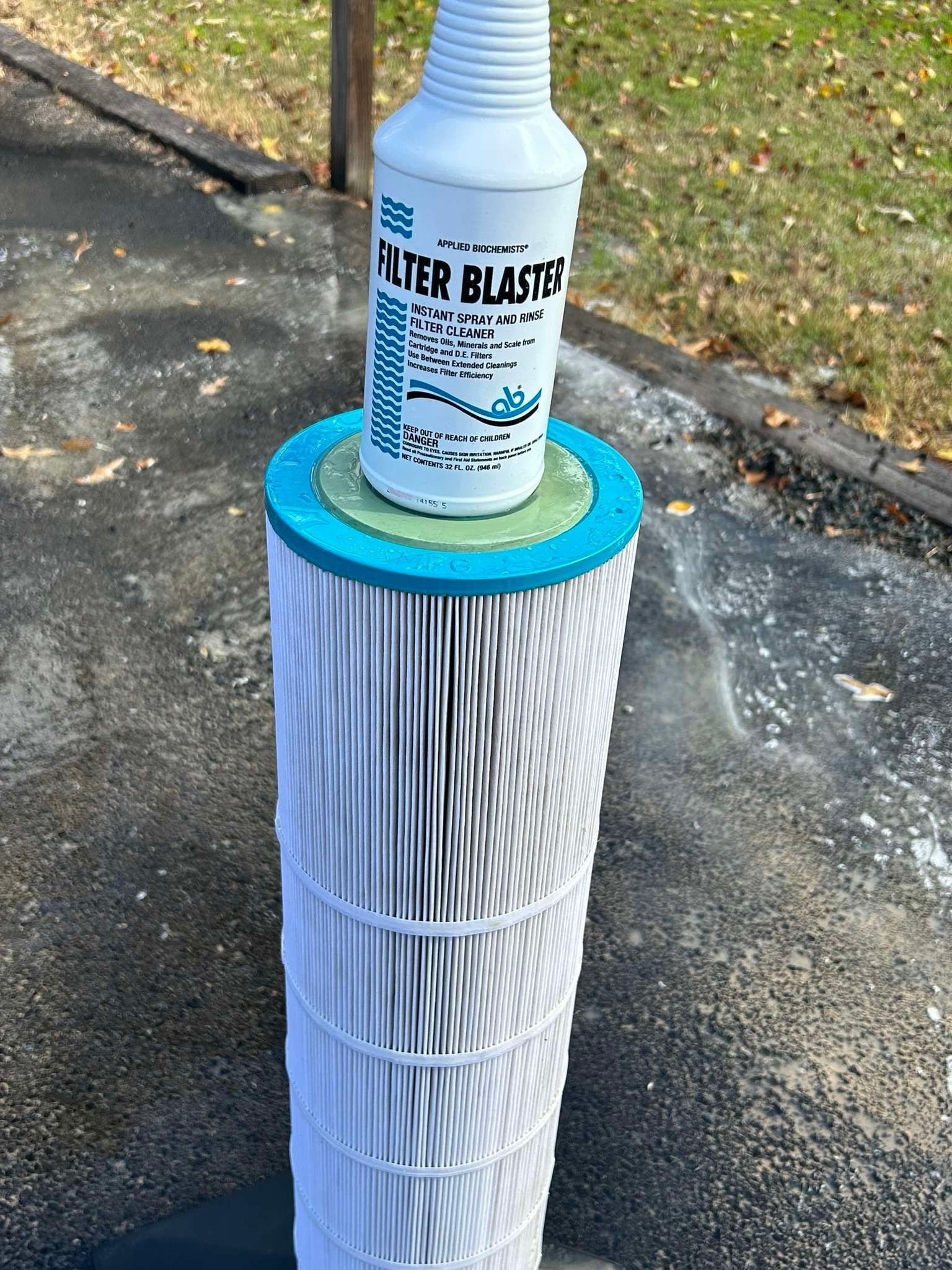 A white cartridge filter with a bottle of filter cleaner on top, outside.
