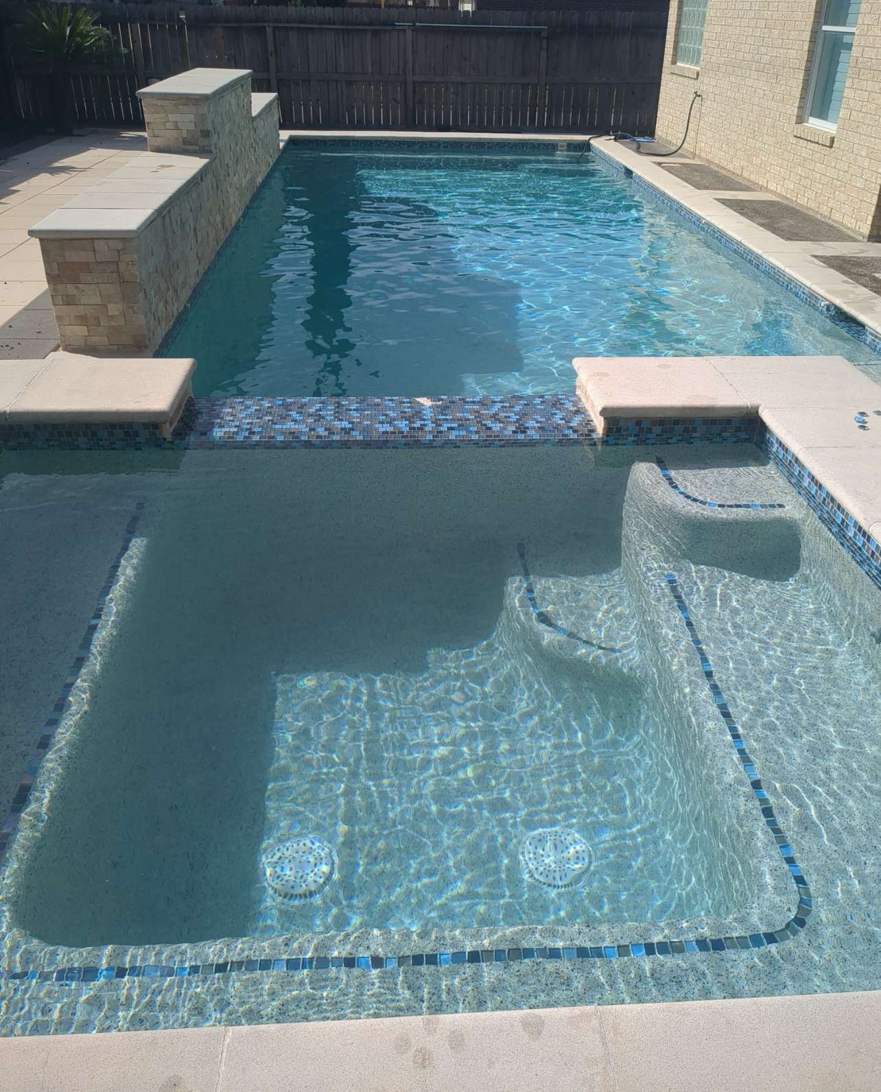 Rectangular swimming pool with attached spa, stone deck, and blue tile trim.