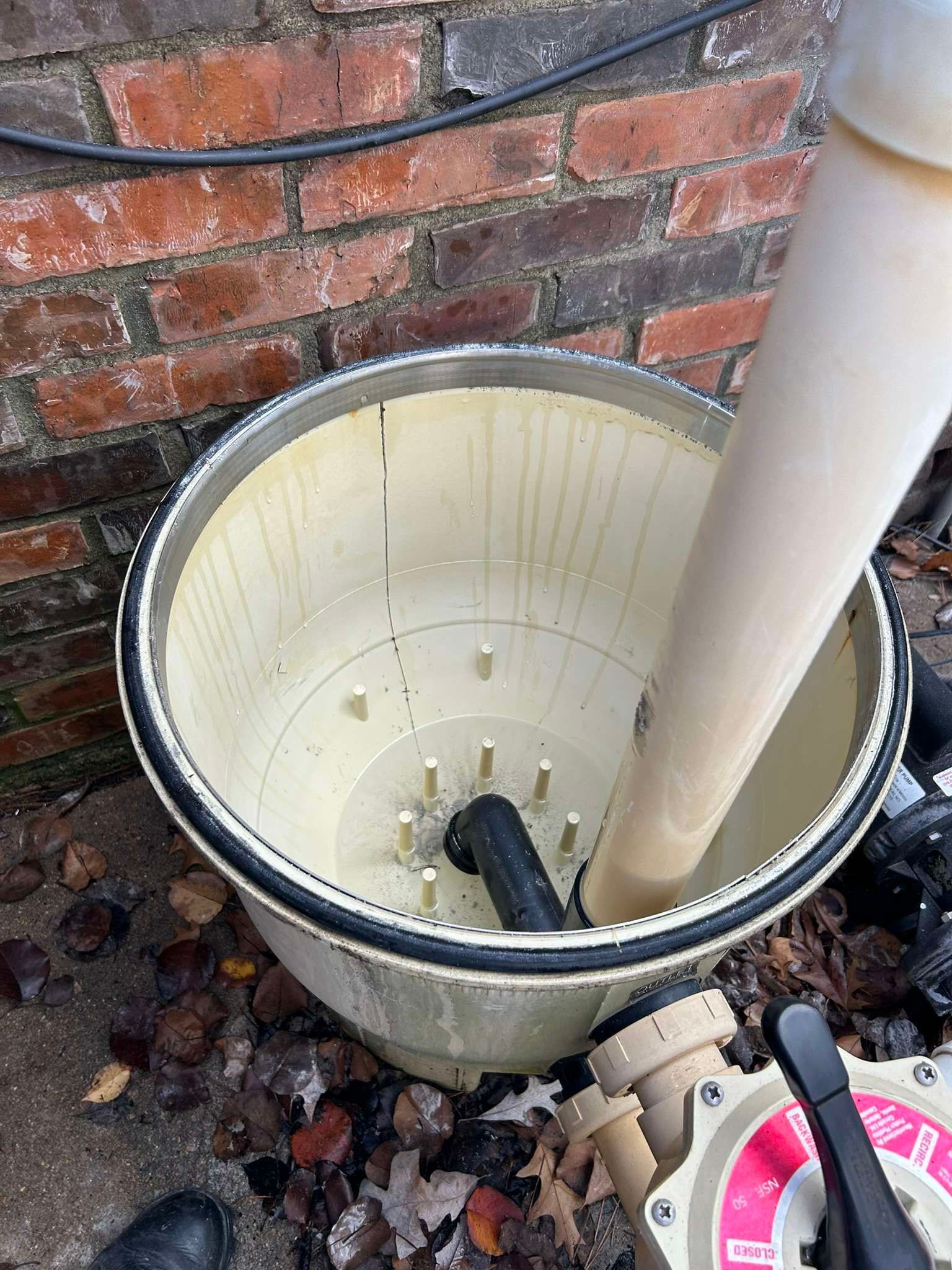 Open pool filter. Beige cylindrical tank, black rubber seal, black inner pipe, connected to a white pipe and valve.