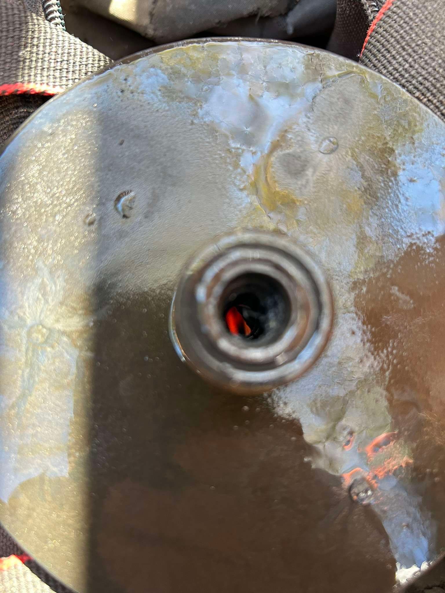 Close-up of a dark, oily metal disc with a central, hollow, circular tube. Reddish hue visible inside the tube.