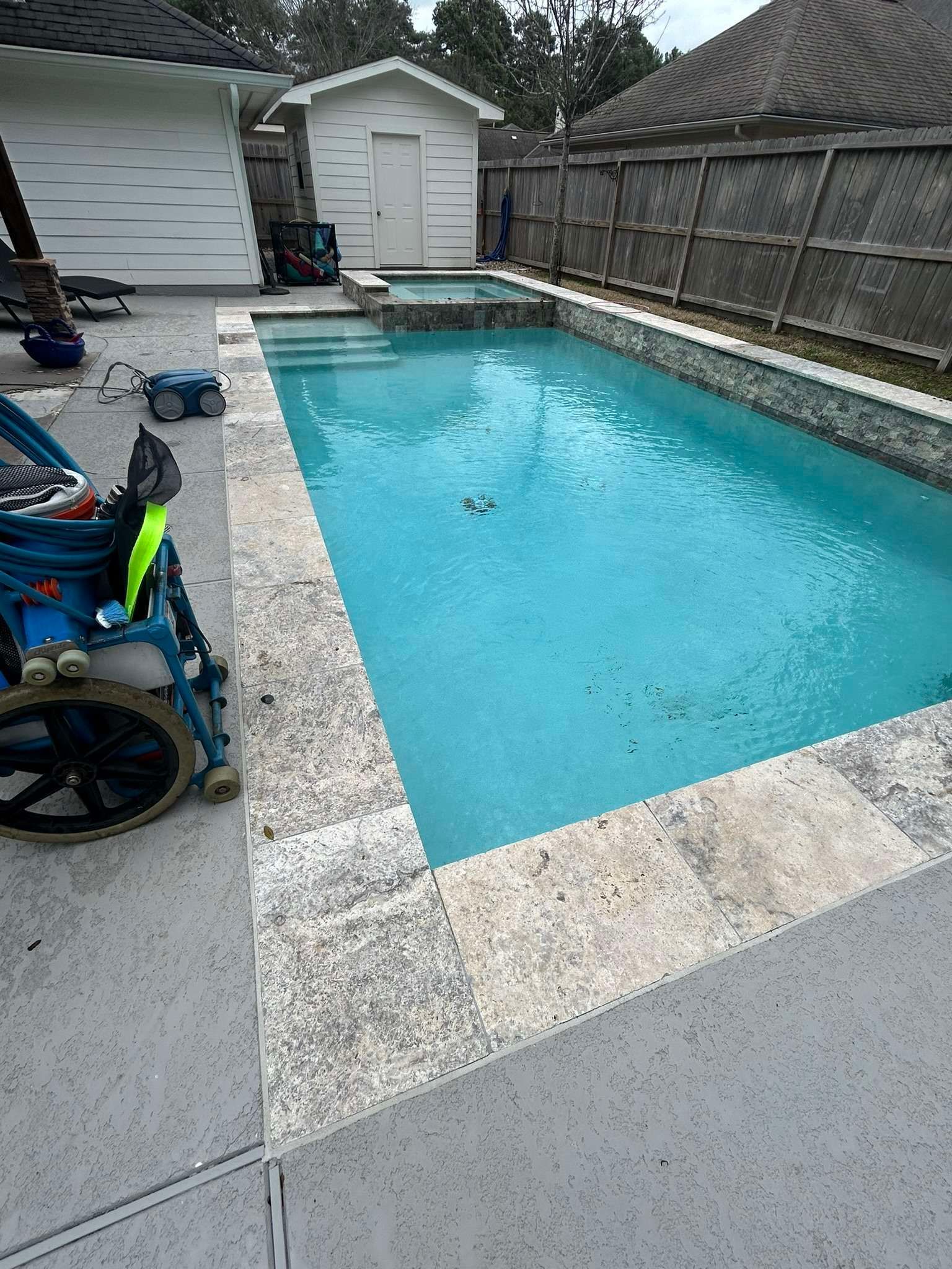 Backyard pool with light blue water and stone border. Tools near edge.