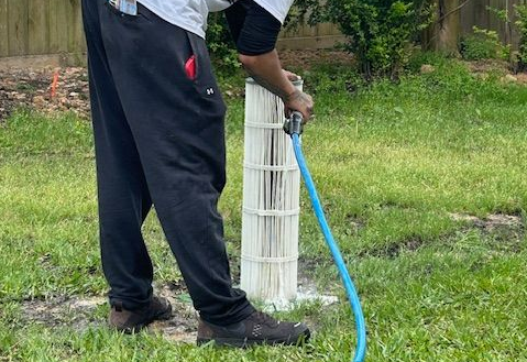 Person attaching filter to a blue above-ground pool; the filter is gray with white hoses.