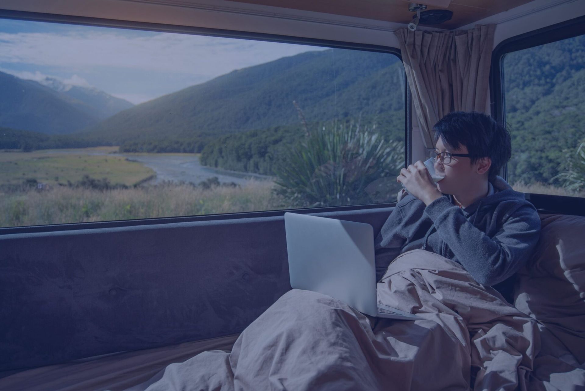 a man is sitting in a van drinking coffee and using a laptop .