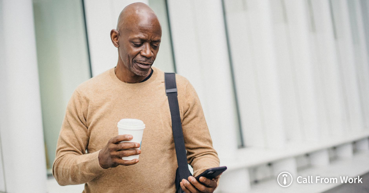 A man is holding a cup of coffee and looking at his cell phone.