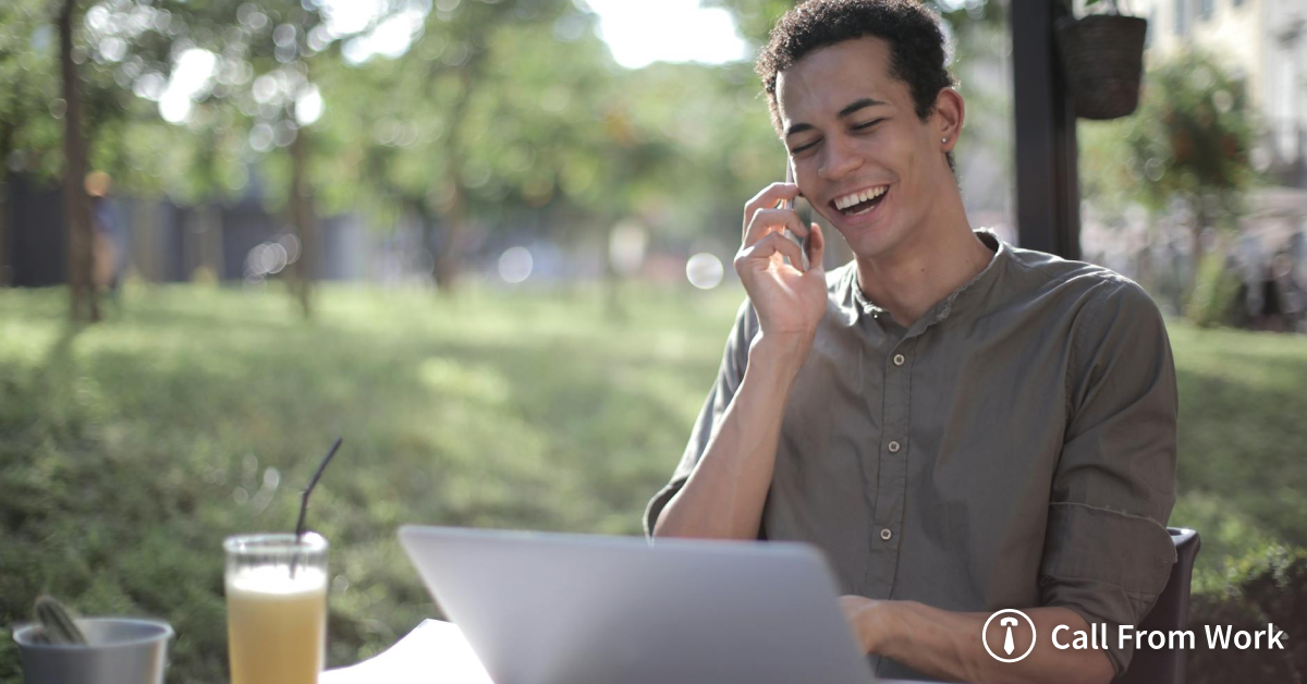 A man is sitting at a table with a laptop and talking on a cell phone.