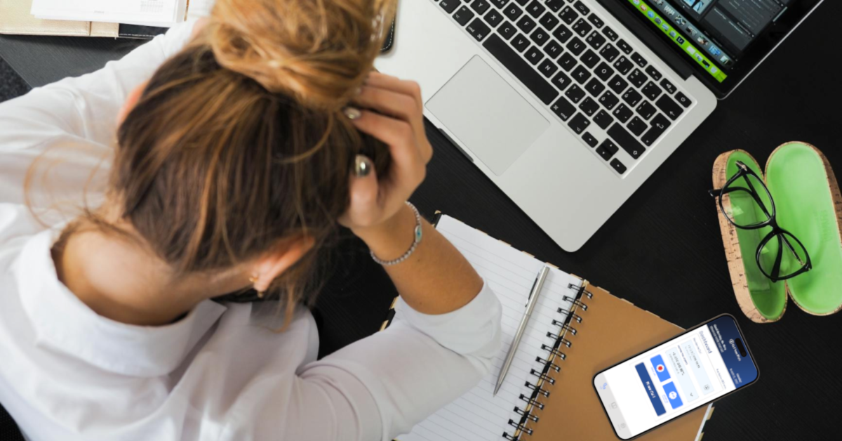 A woman is sitting at a desk with a laptop and a cell phone.