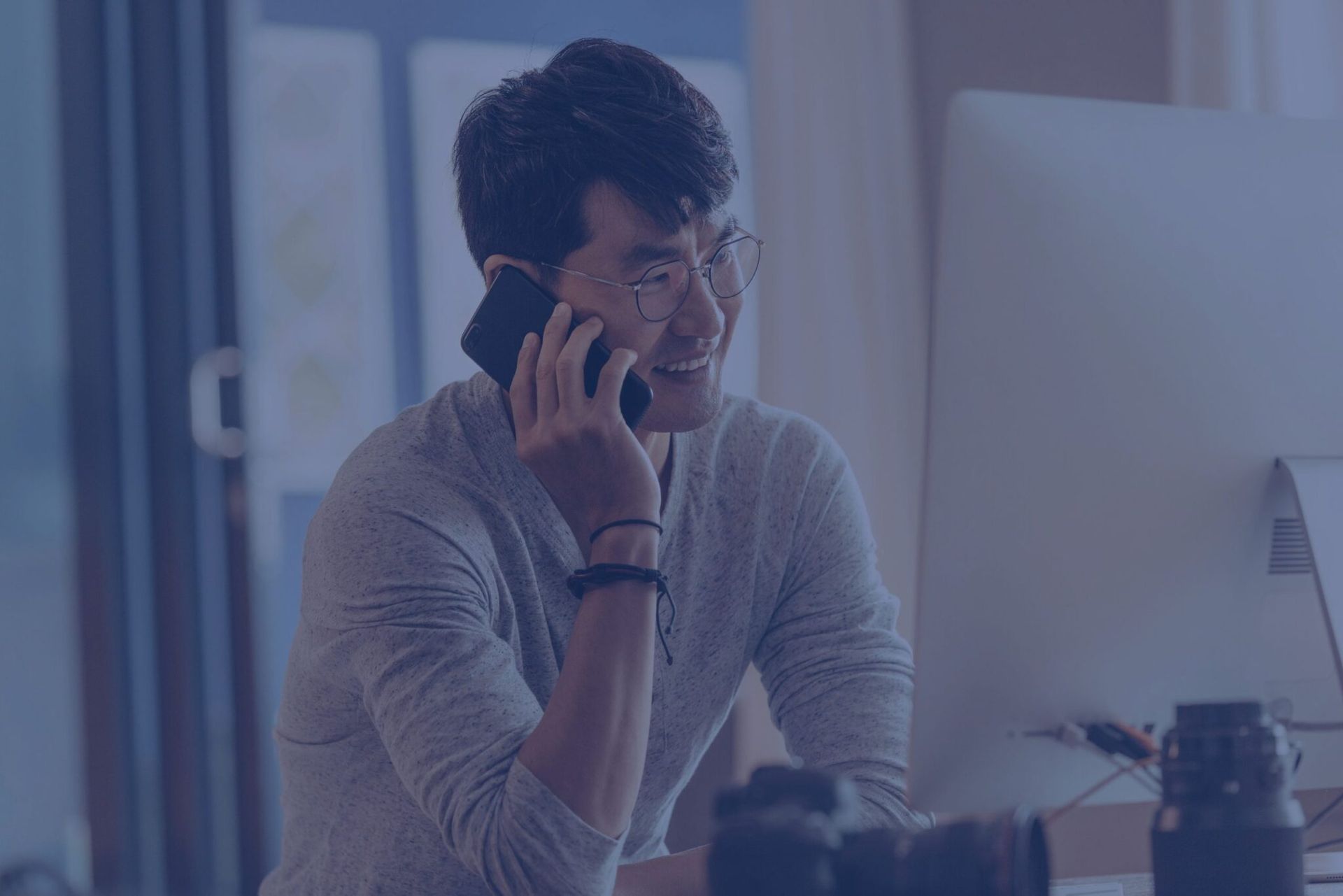 a man is sitting at a desk talking on a cell phone .