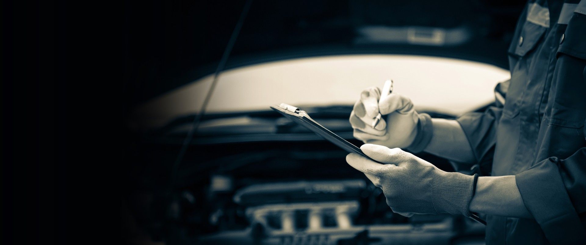 A mechanic is writing on a clipboard while working on a car.
