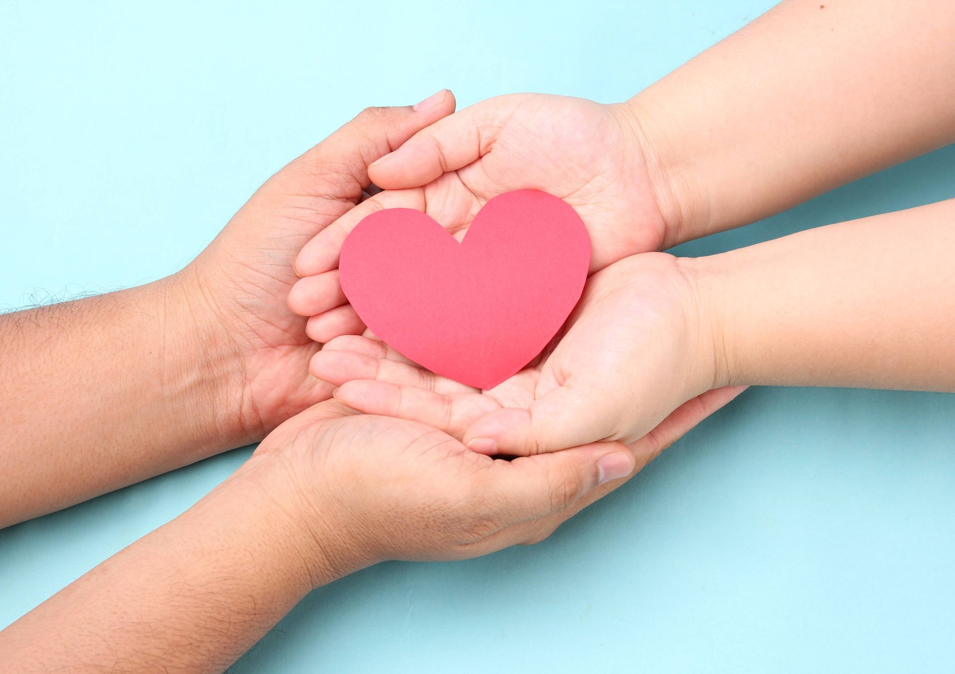 two people are holding a red heart in their hands