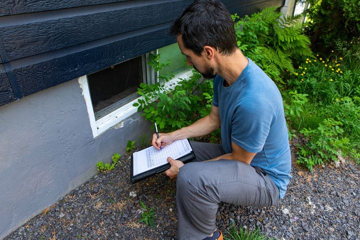 a man is kneeling down in front of a house writing on a clipboard