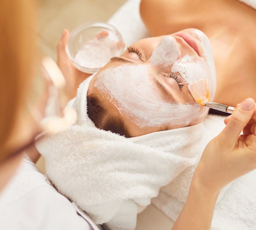 Eine Frau mit einem Handtuch um den Kopf gewickelt bekommt eine Gesichtsbehandlung.