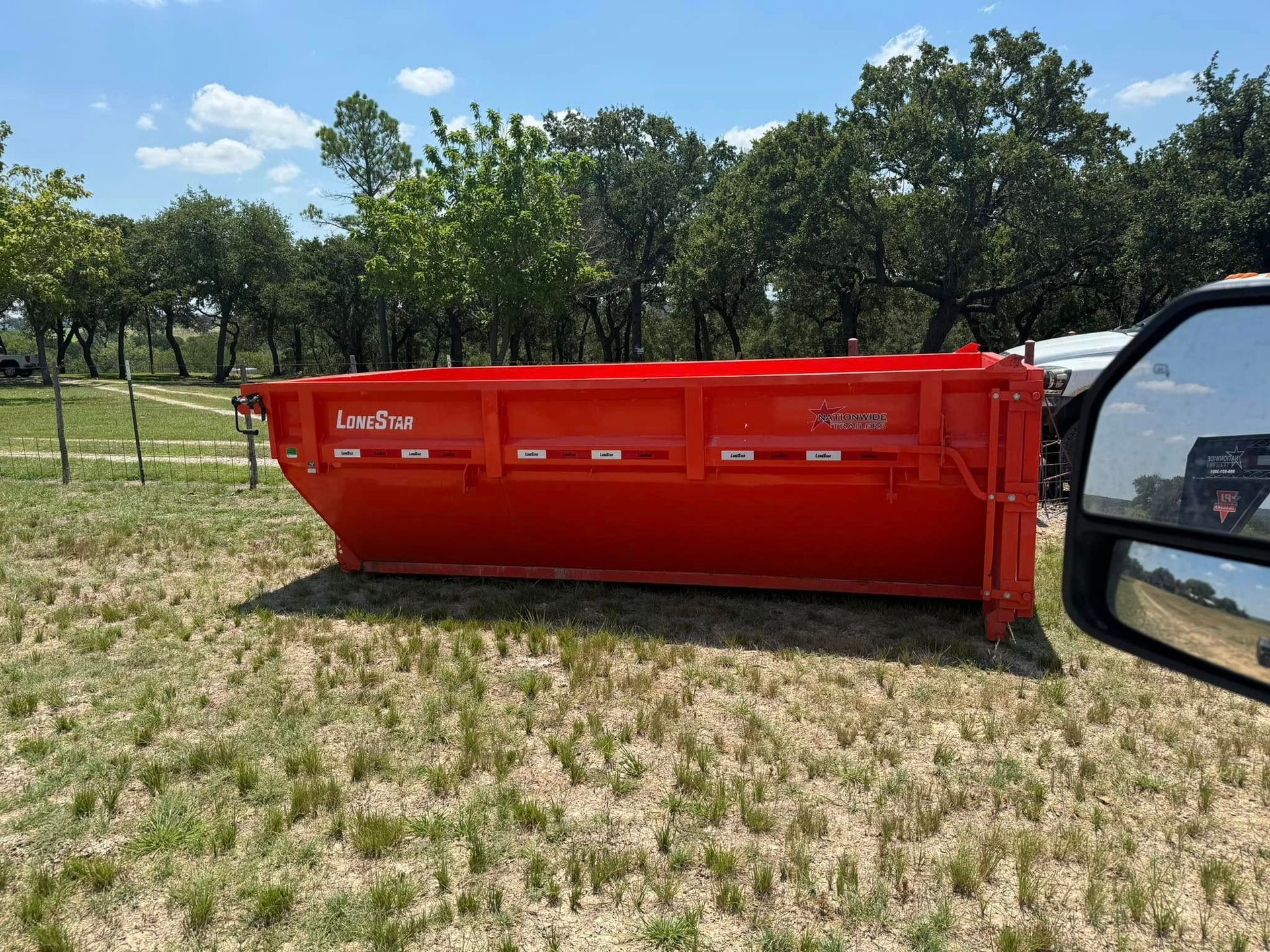 A red dumpster is parked in a grassy field next to a truck.