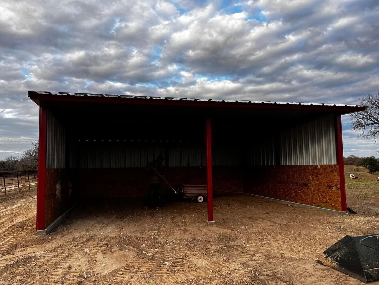 A shed with a red roof is sitting in the middle of a dirt field.