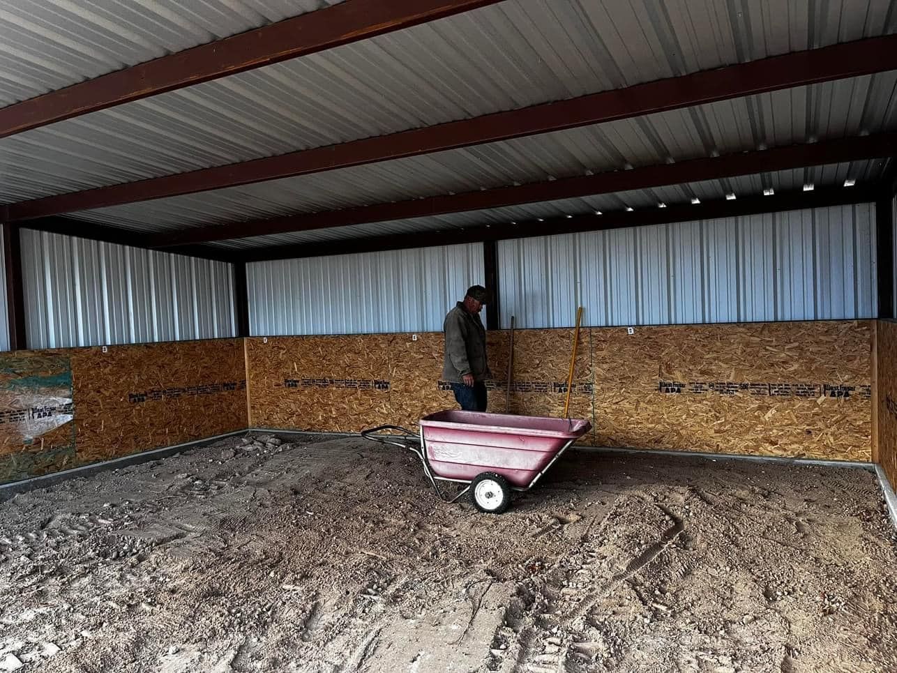 A man is standing next to a wheelbarrow in a shed.