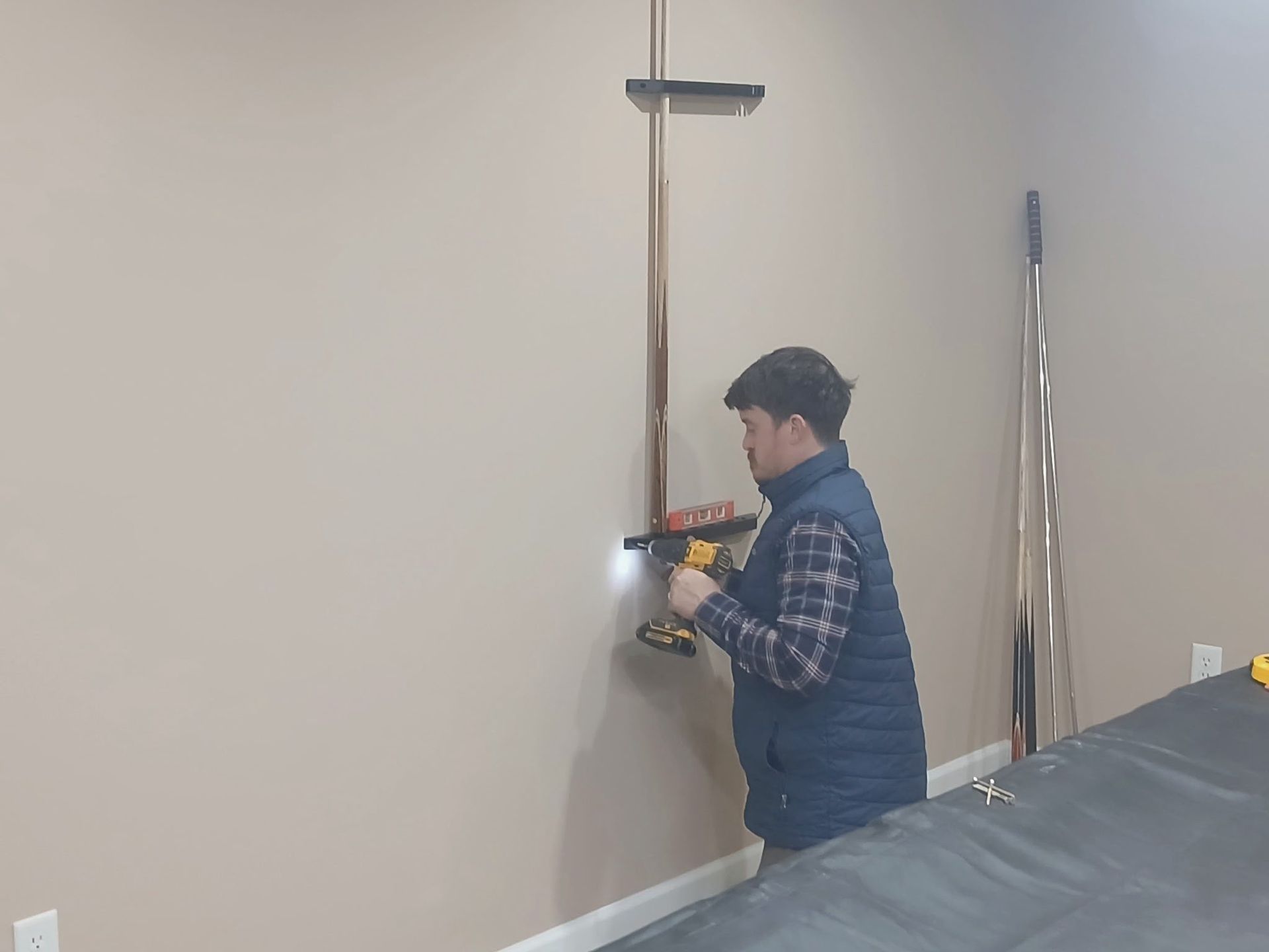 Person using a power drill to mount a bracket on a beige wall in a room