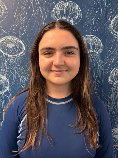 A man in a purple shirt is smiling in front of a wall with jellyfish on it