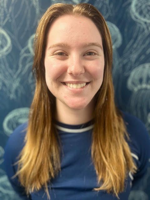 A man in a purple shirt is smiling in front of a wall with jellyfish on it
