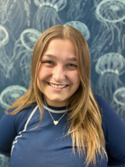 A woman in a blue shirt is smiling in front of a wall with jellyfish on it.