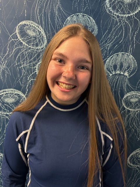 A woman in a blue shirt is smiling in front of a wall with jellyfish on it