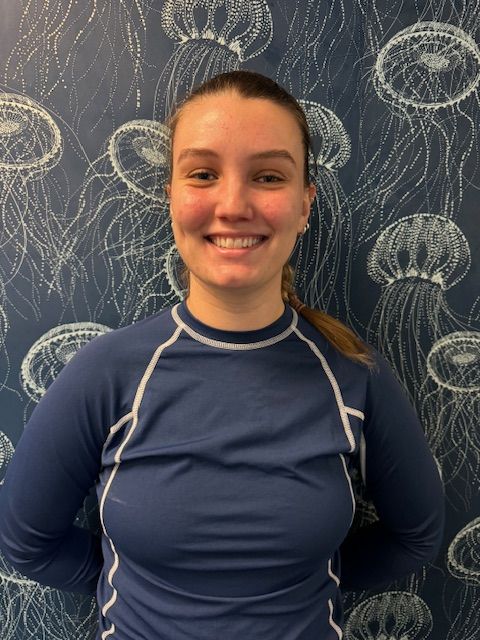 A woman in a blue shirt is smiling in front of a wall with jellyfish on it