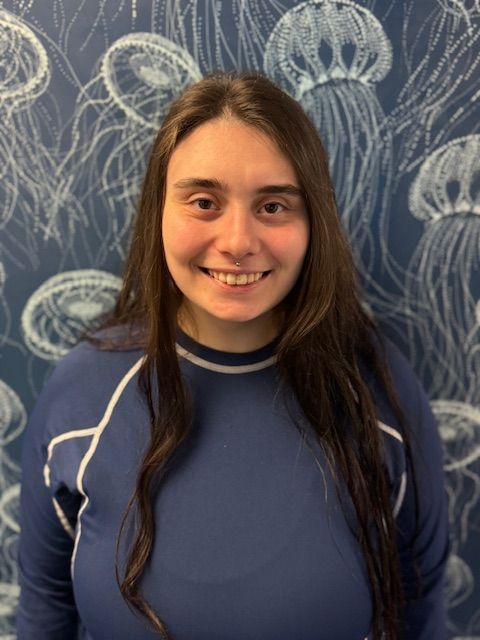 A woman in a blue shirt is smiling in front of a wall with jellyfish on it