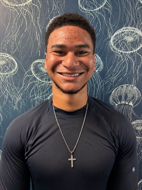 A woman wearing glasses and a blue shirt is standing in front of a wall with jellyfish on it