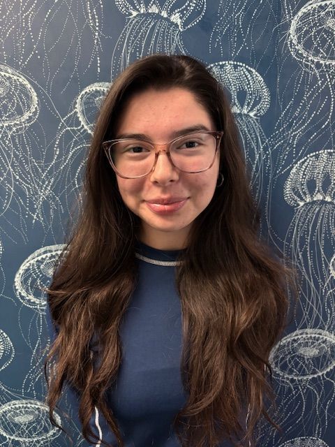 A woman in a blue shirt is smiling in front of a wall with jellyfish on it.