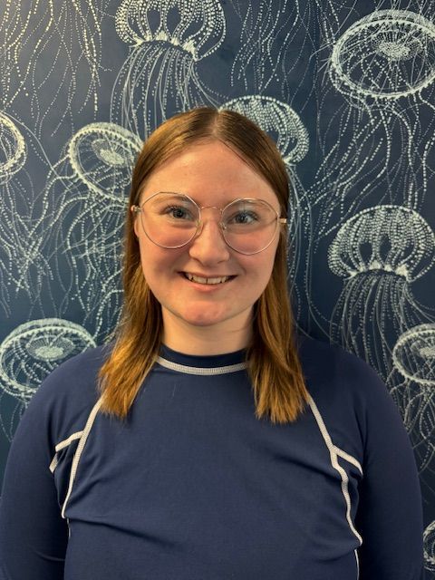 A man in a blue shirt is smiling in front of a wall with jellyfish on it