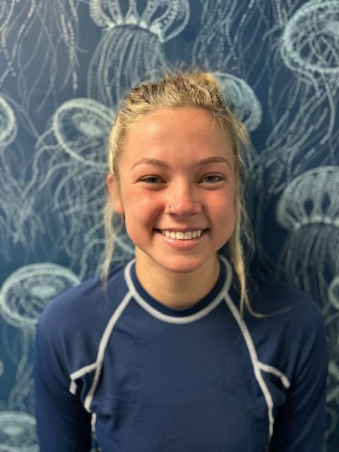 A woman in a blue shirt is smiling in front of a wall with jellyfish on it