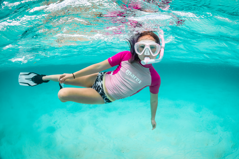 A woman is swimming underwater in the ocean wearing a mask and flippers.