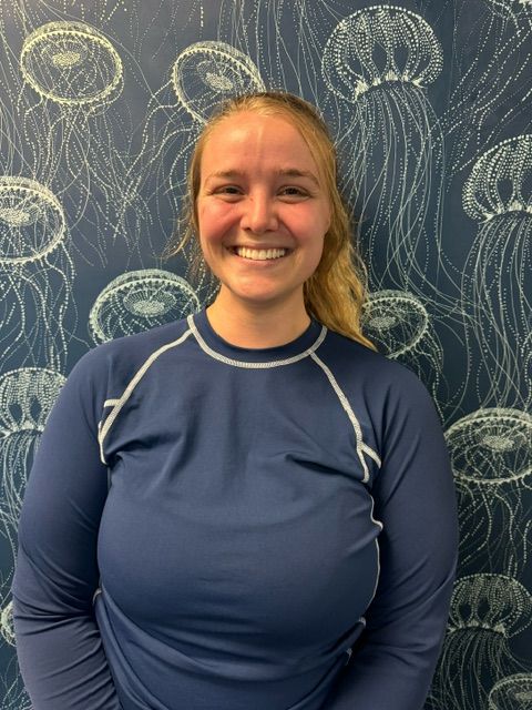 A woman in a blue shirt is smiling in front of a wall with jellyfish on it