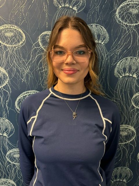 A woman wearing glasses and a blue shirt is standing in front of a wall with jellyfish on it