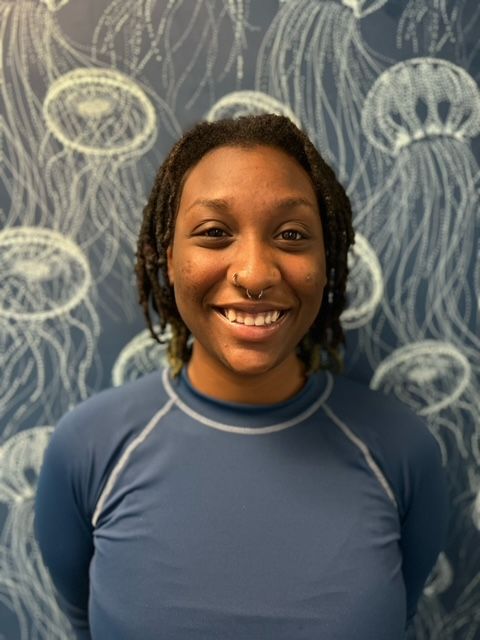 A woman in a blue shirt is smiling in front of a wall with jellyfish painted on it