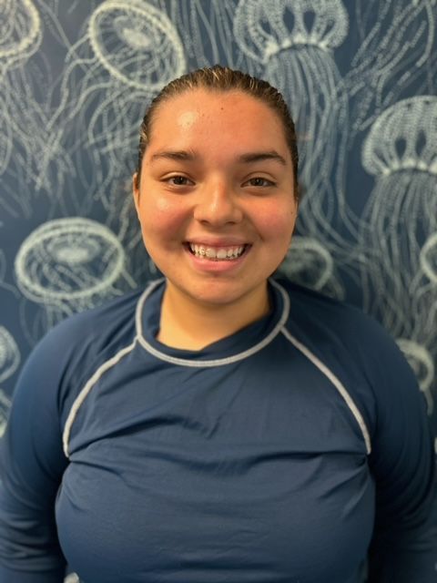 A woman in a blue shirt is smiling in front of a wall with jellyfish on it.