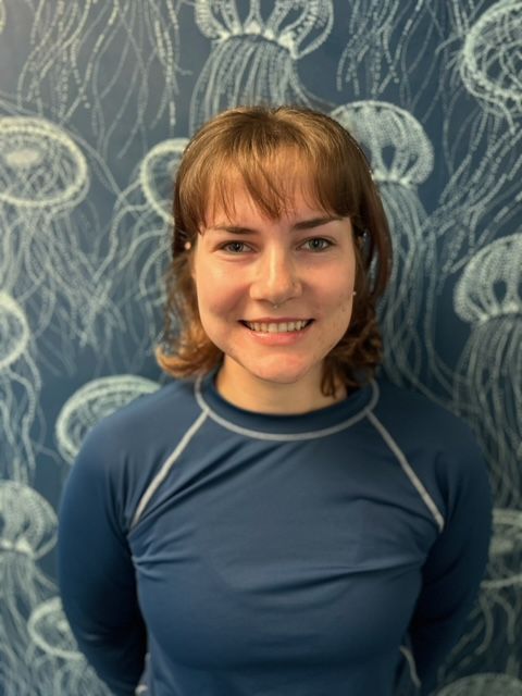 A woman in a blue shirt is smiling in front of a wall with jellyfish on it.