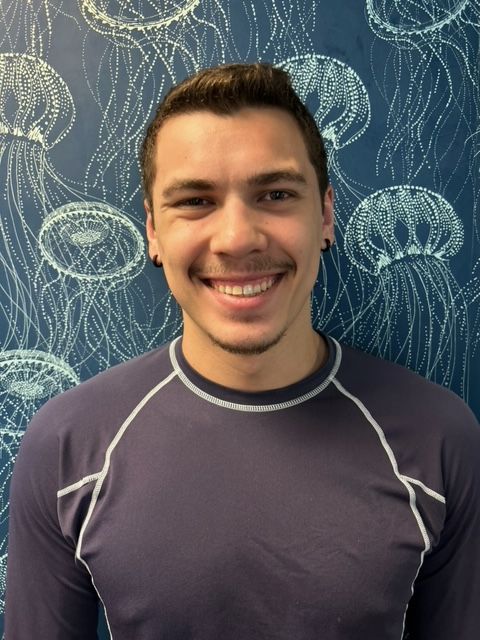 A man in a purple shirt is smiling in front of a wall with jellyfish on it