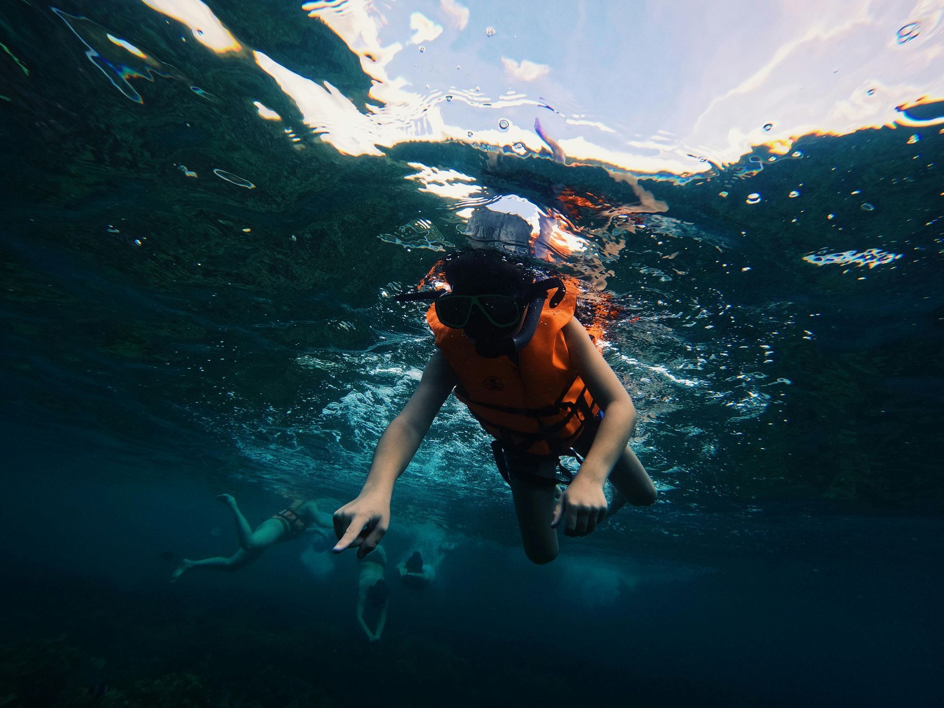 A person is swimming in the ocean wearing a life jacket and mask.