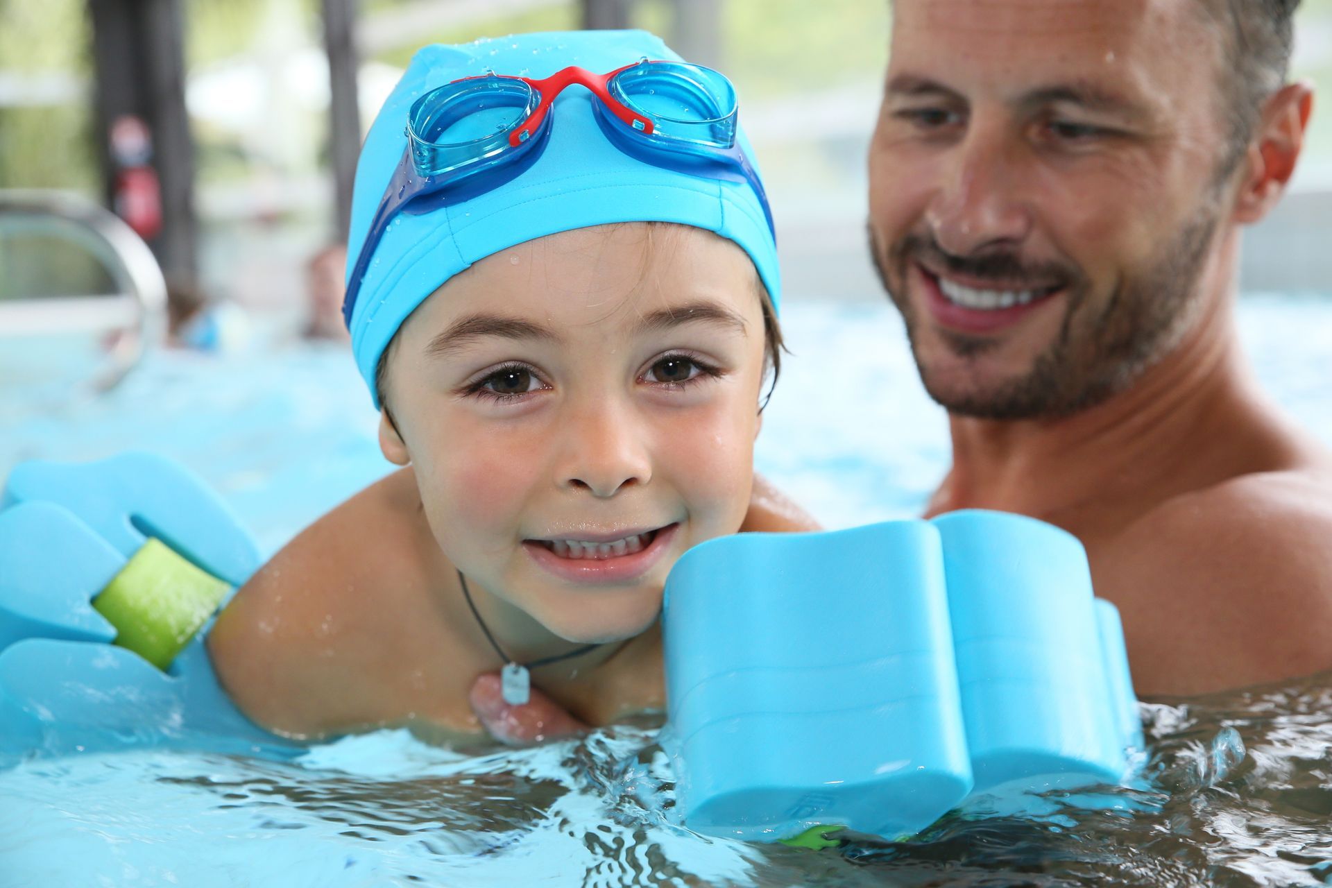 A man is teaching a little boy how to swim in a swimming pool.