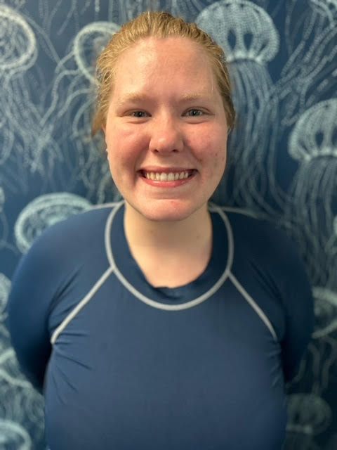 A woman in a blue shirt is smiling in front of a wall with jellyfish on it.