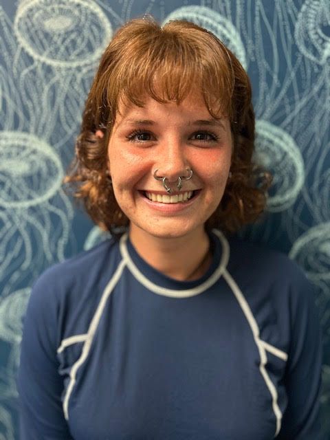 A woman with a nose ring is smiling in front of a wall with jellyfish on it.