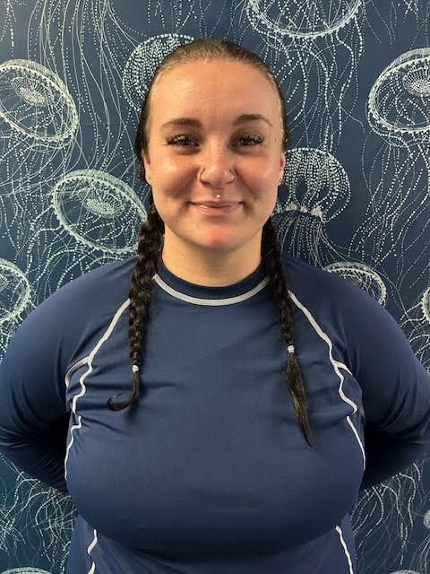 A woman in a blue shirt is smiling in front of a wall with jellyfish on it