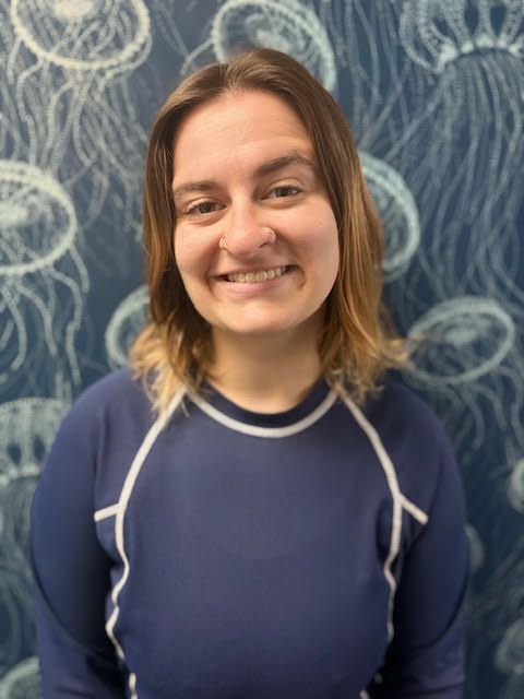 A woman in a blue shirt is smiling in front of a wall with jellyfish on it