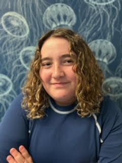 A woman with curly hair is standing in front of a wall with jellyfish painted on it.