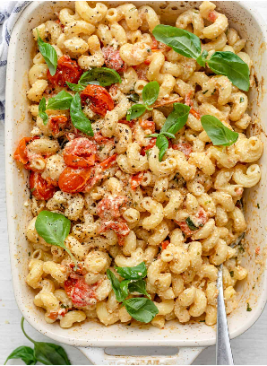 A white casserole dish with a pasta salad made from cherry tomatoes, feta cheese, and basil.