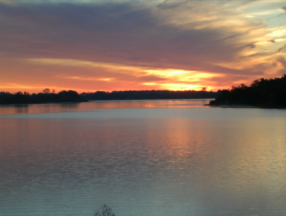 A body of water with trees and a sunset in the background