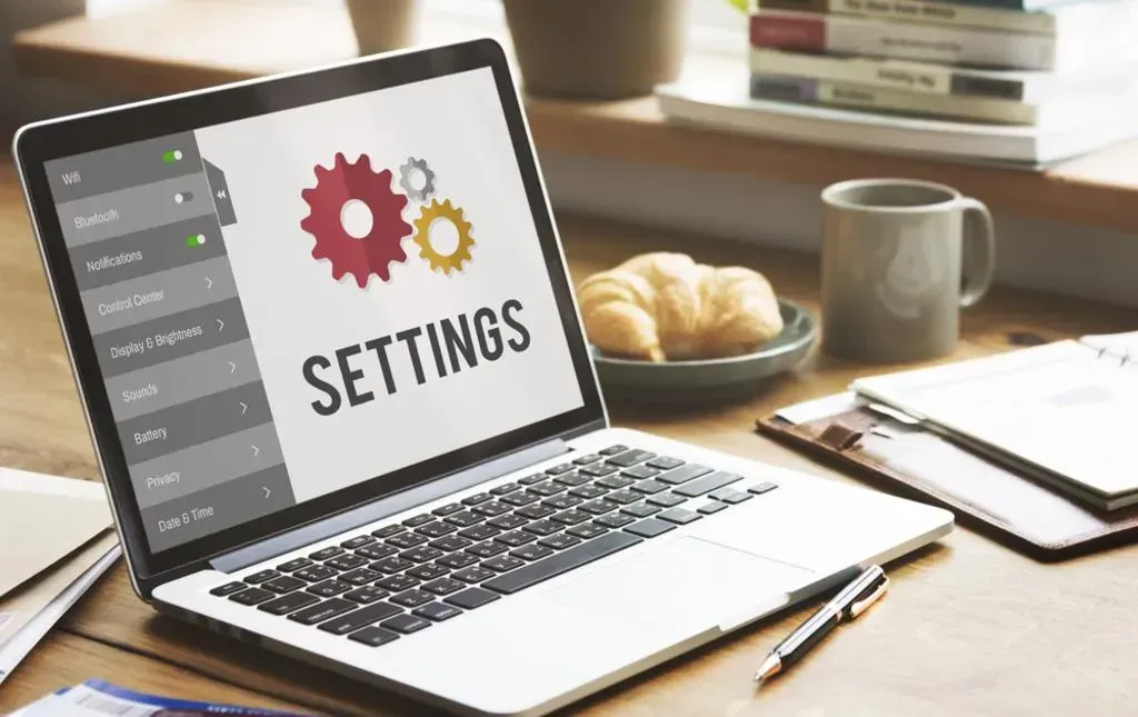 A laptop with the word settings on the screen is sitting on a desk.