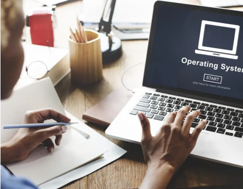 A person is typing on a laptop that says operating system