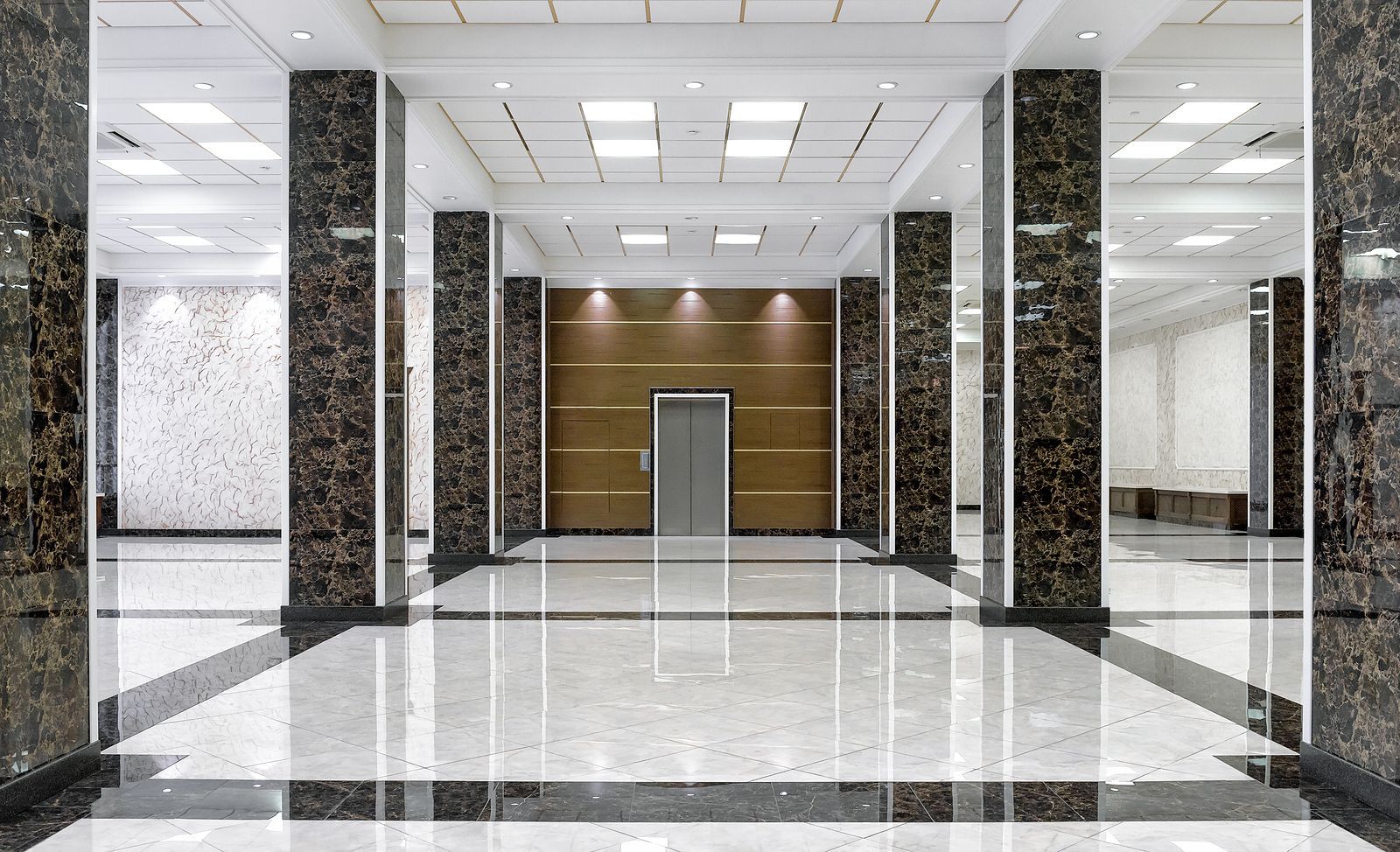 Spacious lobby with marble floors and columns, elevator at the back, recessed lighting.