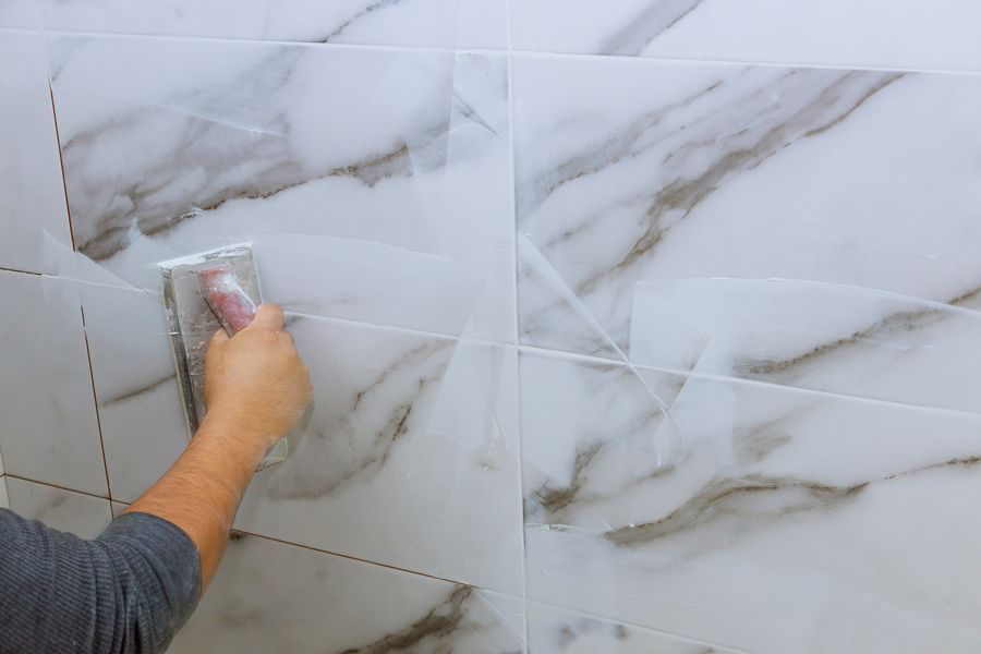 Person grouting white marble tiles with a handheld tool.