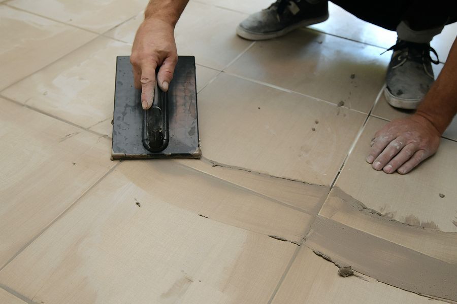 Person applying grout to floor tiles with a trowel.